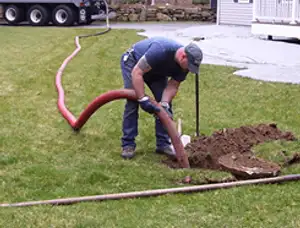 Septic pumping technician servicing a residential septic tank with a vacuum hose in Louisville, KY