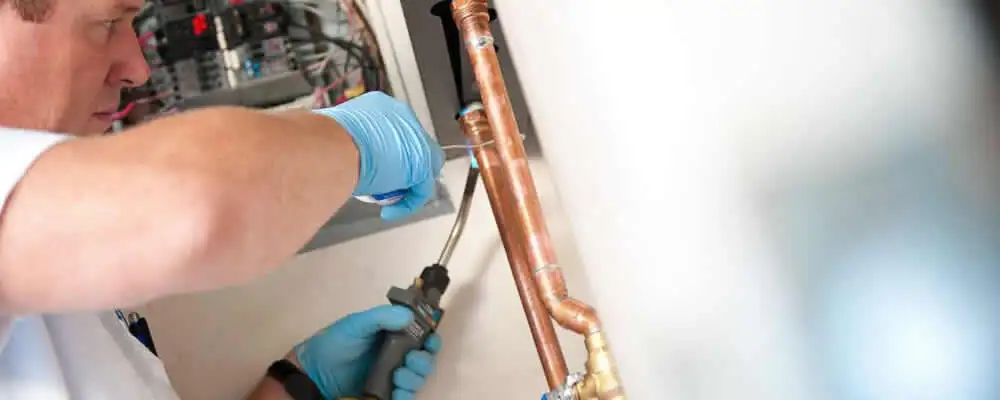 Water heater repair technician testing copper pipe connections and controls in Louisville, KY